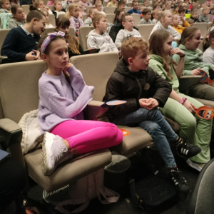 Uczniowie kl. 2 słuchają informacji dotyczących filmu. Dzieci siedzą w fotelach w sali Regionalnego Centrum Kulturalno-Bibliotecznego w Brzesku. Kliknięcie na zdjęcie spowoduje jego powiększenie do rozmiaru oryginalnego